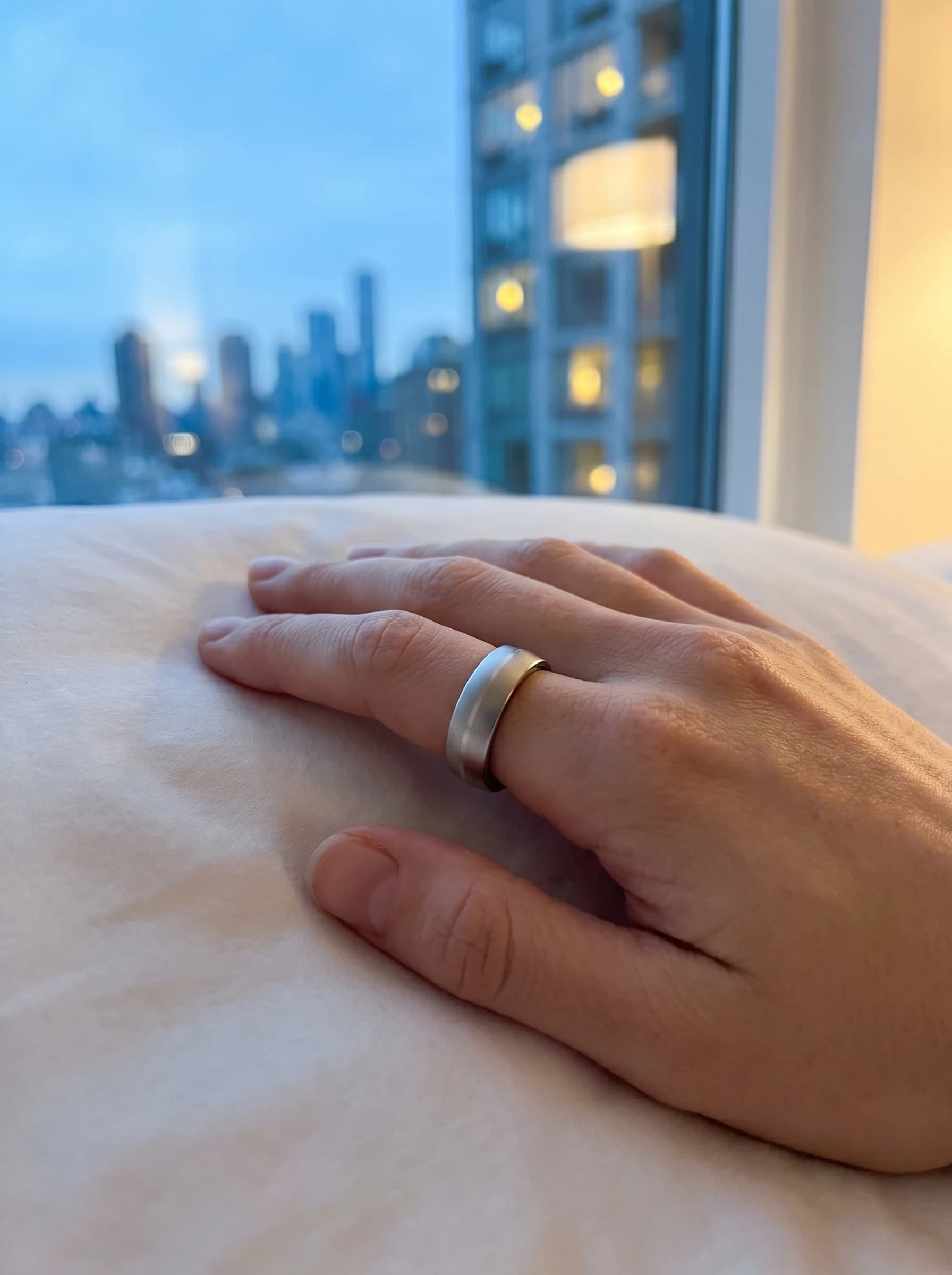 Main avec bague SKY sur le lit, skyline dans la lumière du matin